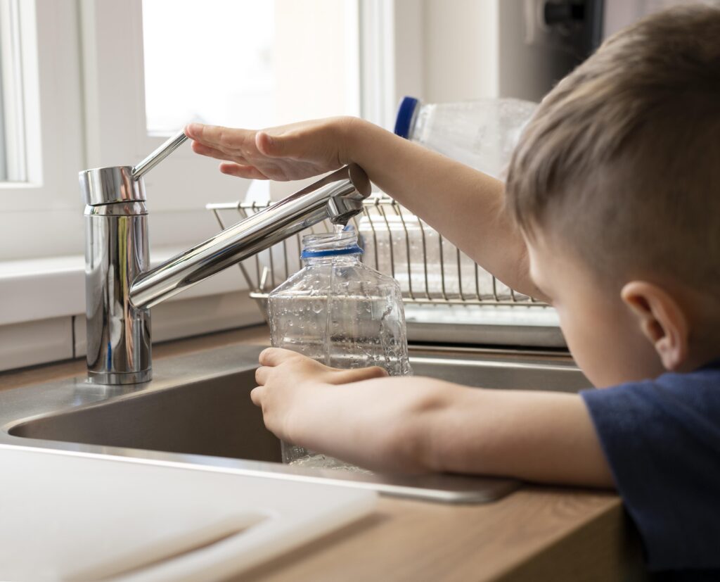 Analisi acqua potabile: bambino che riempie una bottiglia d'acqua dal rubinetto